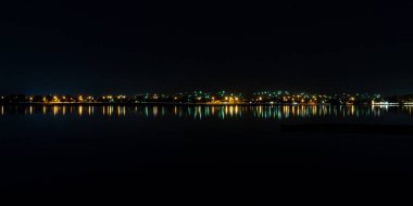Gece lambaları Ballarat 'taki Wendouree Gölü kıyısı boyunca bulanık çizgileri yansıtıyor.