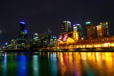 Melbourne City ve Flinders caddelerinin renkli rıhtımı. Suyun üzerinde yansıyan ışıklarla tarihi bina.