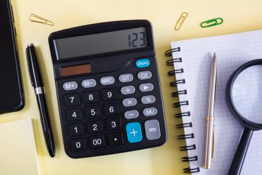 Sarı bir yüzeyde hesap makinesi, defter ve kalem.
