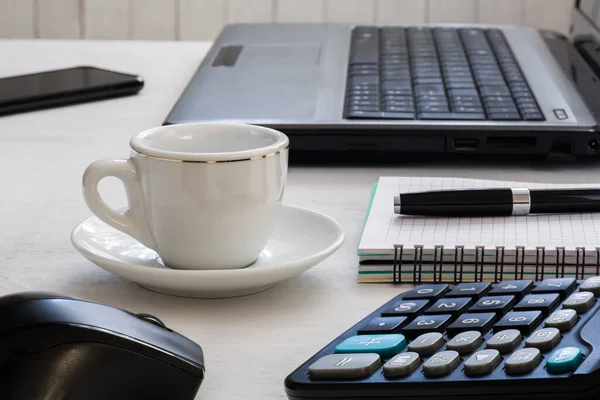 Desktop: laptop, notebook with pen, cup of coffee, calculator and smartphone