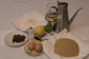 Chiffon cake ingredients, glass of Moscato d'Asti, lemons, raisins, brown sugar, flour 00, on background of white fabric, full frame Nikon d750
