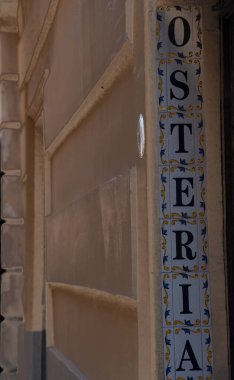 Osteria tabelasının beyaz arka planda mavi harflerle ve sarı ve mavi yapraklarla süslenmiş fayansları..