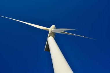 Mavi gökyüzünün arka planına karşı duran bir rüzgar jeneratörünün yakın plan görüntüsü. Çevreyi koruyan ve yeşil enerji üreten türbin..