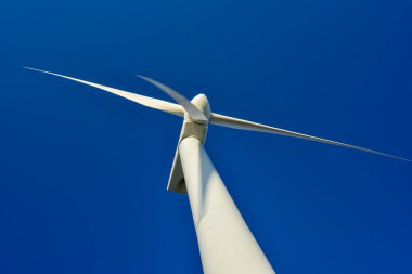 Mavi gökyüzünün arka planına karşı duran bir rüzgar jeneratörünün yakın plan görüntüsü. Çevreyi koruyan ve yeşil enerji üreten türbin..