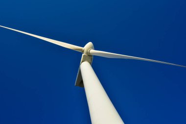 Mavi gökyüzünün arka planına karşı duran bir rüzgar jeneratörünün yakın plan görüntüsü. Çevreyi koruyan ve yeşil enerji üreten türbin..