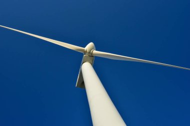 Mavi gökyüzünün arka planına karşı duran bir rüzgar jeneratörünün yakın plan görüntüsü. Çevreyi koruyan ve yeşil enerji üreten türbin..