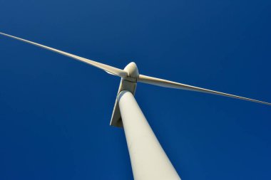 Mavi gökyüzünün arka planına karşı duran bir rüzgar jeneratörünün yakın plan görüntüsü. Çevreyi koruyan ve yeşil enerji üreten türbin..