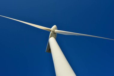 Mavi gökyüzünün arka planına karşı duran bir rüzgar jeneratörünün yakın plan görüntüsü. Çevreyi koruyan ve yeşil enerji üreten türbin..
