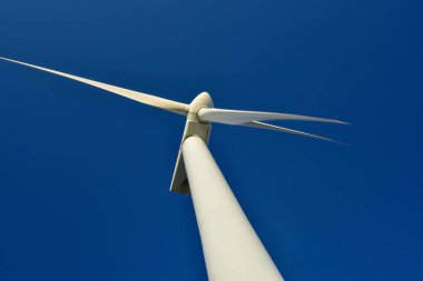 Mavi gökyüzünün arka planına karşı duran bir rüzgar jeneratörünün yakın plan görüntüsü. Çevreyi koruyan ve yeşil enerji üreten türbin..