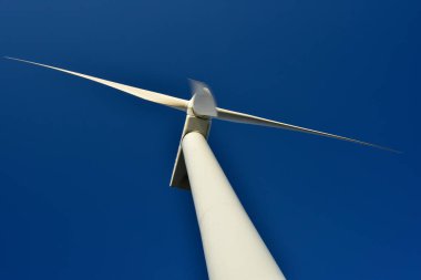 Mavi gökyüzünün arka planına karşı duran bir rüzgar jeneratörünün yakın plan görüntüsü. Çevreyi koruyan ve yeşil enerji üreten türbin..