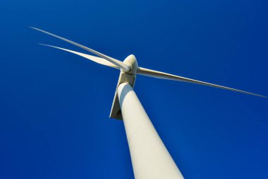 Mavi gökyüzünün arka planına karşı duran bir rüzgar jeneratörünün yakın plan görüntüsü. Çevreyi koruyan ve yeşil enerji üreten türbin..