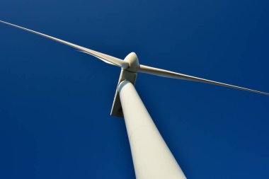 Mavi gökyüzünün arka planına karşı duran bir rüzgar jeneratörünün yakın plan görüntüsü. Çevreyi koruyan ve yeşil enerji üreten türbin..