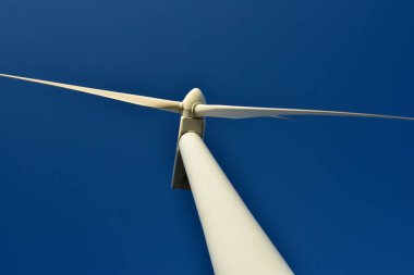 Mavi gökyüzünün arka planına karşı duran bir rüzgar jeneratörünün yakın plan görüntüsü. Çevreyi koruyan ve yeşil enerji üreten türbin..