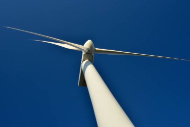 Mavi gökyüzünün arka planına karşı duran bir rüzgar jeneratörünün yakın plan görüntüsü. Çevreyi koruyan ve yeşil enerji üreten türbin..
