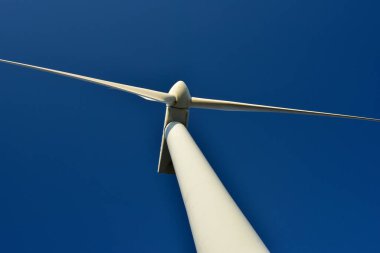 Mavi gökyüzünün arka planına karşı duran bir rüzgar jeneratörünün yakın plan görüntüsü. Çevreyi koruyan ve yeşil enerji üreten türbin..