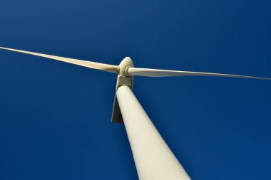 Mavi gökyüzünün arka planına karşı duran bir rüzgar jeneratörünün yakın plan görüntüsü. Çevreyi koruyan ve yeşil enerji üreten türbin..