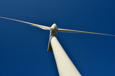Mavi gökyüzünün arka planına karşı duran bir rüzgar jeneratörünün yakın plan görüntüsü. Çevreyi koruyan ve yeşil enerji üreten türbin..