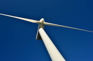 Mavi gökyüzünün arka planına karşı duran bir rüzgar jeneratörünün yakın plan görüntüsü. Çevreyi koruyan ve yeşil enerji üreten türbin..