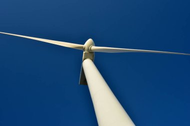 Mavi gökyüzünün arka planına karşı duran bir rüzgar jeneratörünün yakın plan görüntüsü. Çevreyi koruyan ve yeşil enerji üreten türbin..