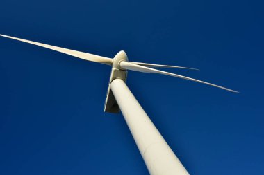 Mavi gökyüzünün arka planına karşı duran bir rüzgar jeneratörünün yakın plan görüntüsü. Çevreyi koruyan ve yeşil enerji üreten türbin..