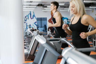 Spor salonunda koşu bandı üzerinde çalışan insanlar