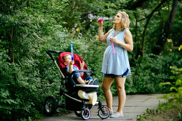 Mulher grávida feliz soprando bolhas de sabão com criança — Fotografia de Stock