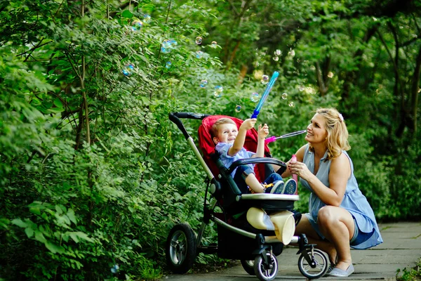 Happy pregnant woman blowing soap bubbles with child — Stock Photo, Image