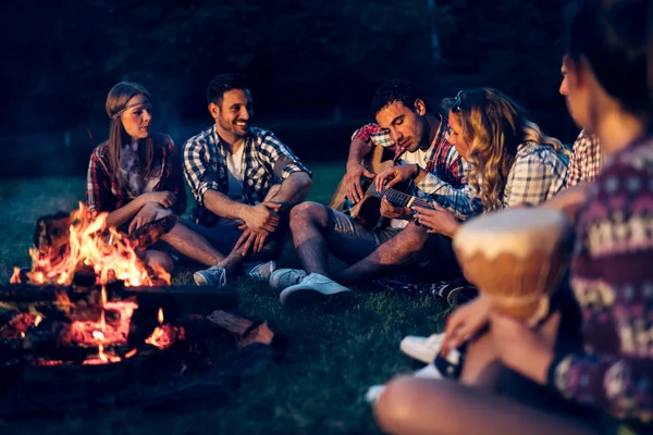 Vänner njuter musik nära lägerelden — Stockfoto