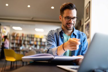 Üniversite kütüphanesinde dizüstü bilgisayarı olan bir erkek öğrenci.