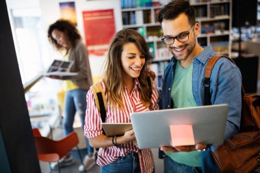 Bir grup mutlu üniversite öğrencisi okul kütüphanesinde okuyor.