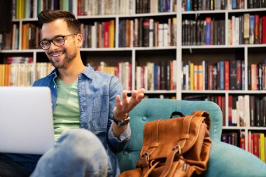 Sınav hazırlayan ve okul kütüphanesinde öğrenim dersleri alan öğrenci, dizüstü bilgisayarda araştırma yapıyor ve internette geziniyor