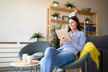 Evinde tablet bilgisayarla dinlenen neşeli genç ve güzel bir kadın.