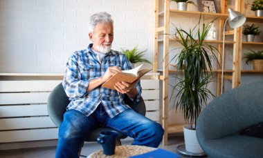 Evde kitap okuyan mutlu yetişkin adam.