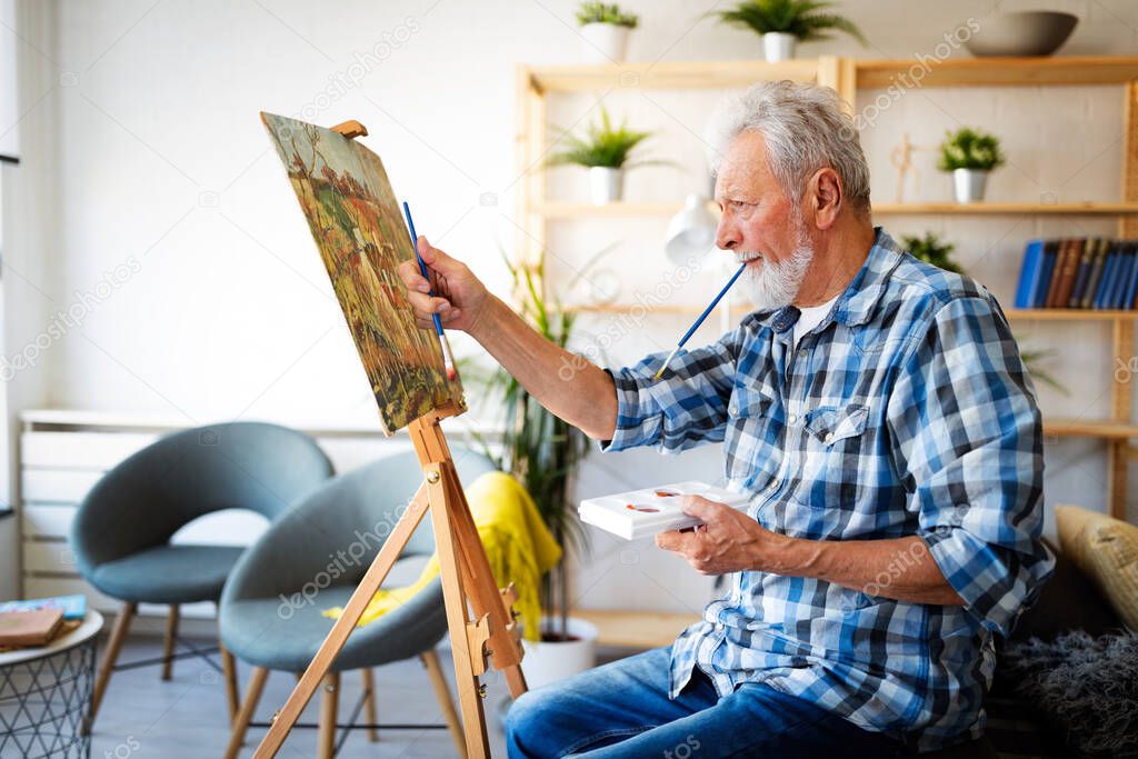 Smiling senior man painting on canvas at home