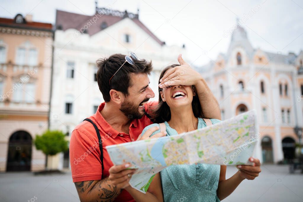 Happy couple walking, smiling, having fun outdoors sightseeing and holding a map