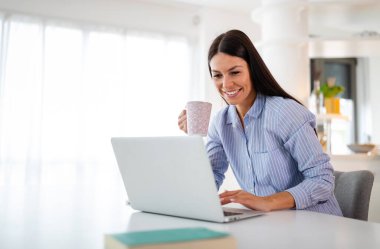 Mutfakta elinde bardak ve defteri olan bir kadın var. Karantina karantinasında evden çalışıyor. Sosyal uzaklık