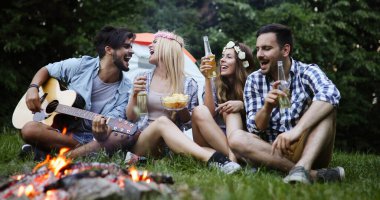 Mutlu arkadaşlar müzik çalıyor ve doğada şenlik ateşinin keyfini çıkarıyorlar.