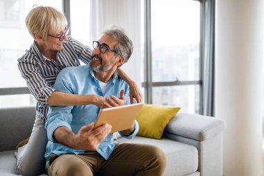 Mutlu yaşlı çift evde dijital tablet kullanıyor.