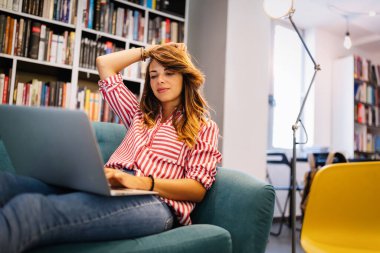 Kanepede otururken dizüstü bilgisayar kullanan mutlu bir kadın.