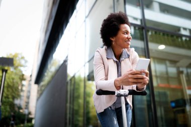 Scooter 'ın yanında duran ve şehirde cep telefonu kullanan mutlu kadın.