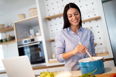 Genç bir kadın evde yemek pişirmeyi internetten öğrenmeye çalışıyor.