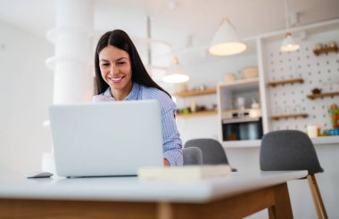 Güzel genç bir bayan çalışıyor, evde laptopuyla çalışıyor.