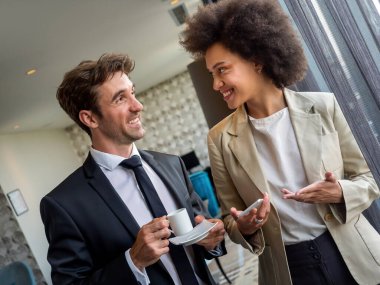 Kahve molası. Resmi olarak iş yerinde sohbet eden, pencerenin yanında kahve içen iki genç meslektaşım var.