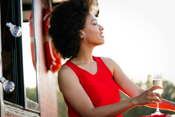 Lifestyle fashion portrait of stunning black woman resting outdoor. Glass in hand. Drinking champagne.