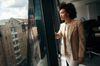 Ofisin penceresinden bakan çekici siyahi iş kadını.