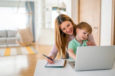 Annesi laptopunda oğluyla birlikte evde çalışıyor.