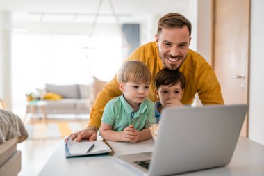 Yakışıklı baba ve çocukları dizüstü bilgisayar kullanıyorlar ve evde yatakta birlikte yatarken gülümsüyorlar.
