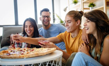 Neşeli çok ırklı arkadaşlar evde pizza yerken eğleniyorlar.