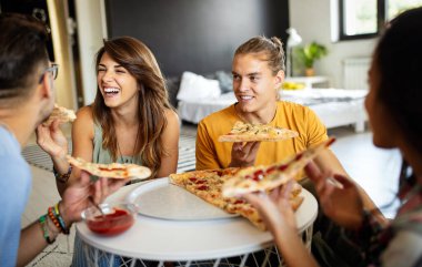 Neşeli çok ırklı arkadaşlar evde pizza yerken eğleniyorlar.