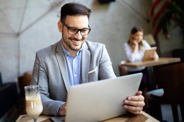 Ofiste dizüstü bilgisayar kullanarak çalışan yakışıklı, kendine güvenen iş adamı.